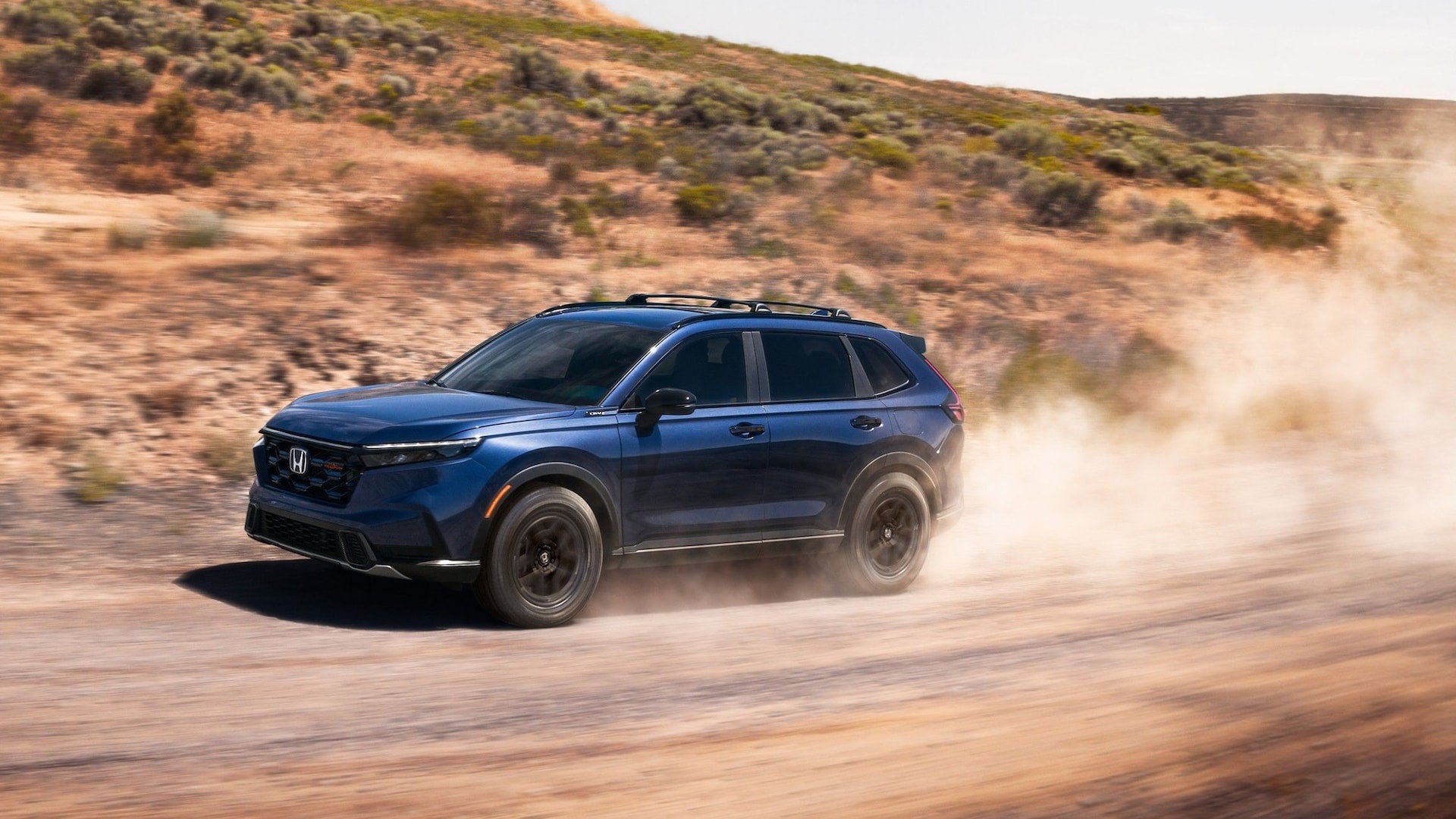 A blue 2026 Honda CR-V driving along a dirt road in a desert, kicking up dirt