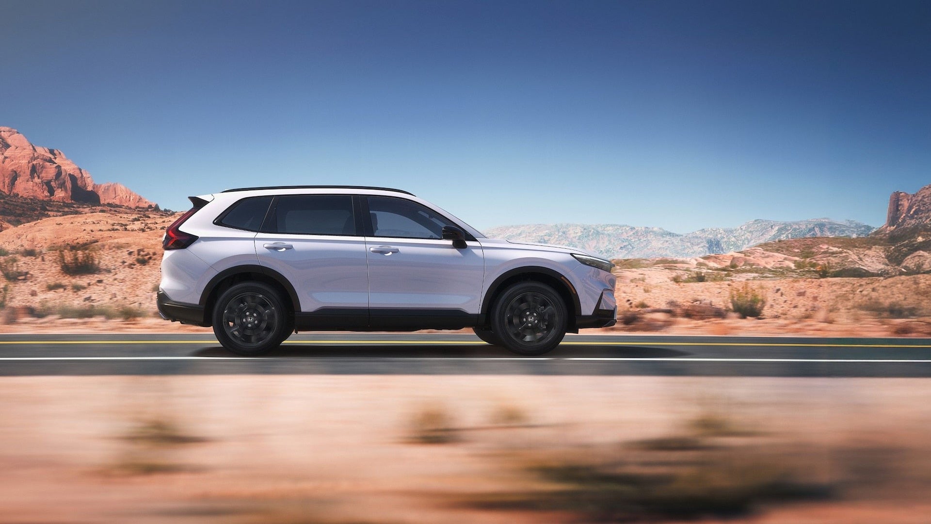 A silver Honda CR-V in profile, driving down the road in a desert