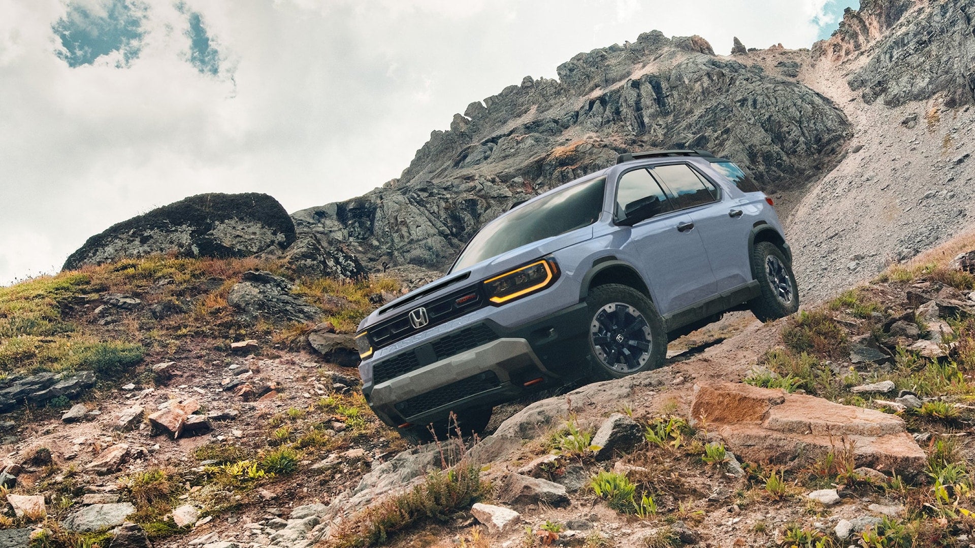 A light blue Honda Passport driving down a dirt road on a small mountain