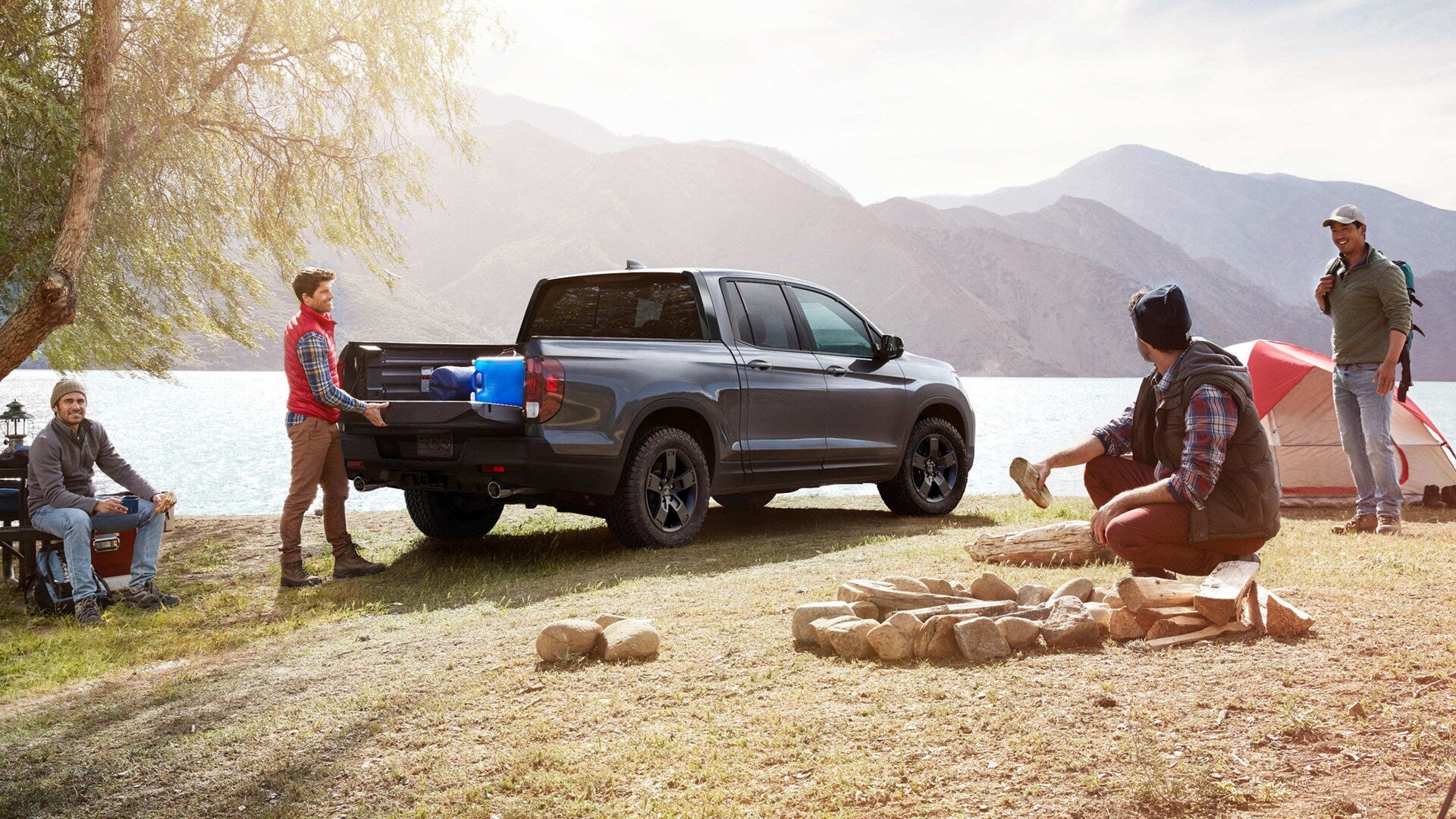 A gray Honda Ridgeline parked at a campsite by a lake with a group of men