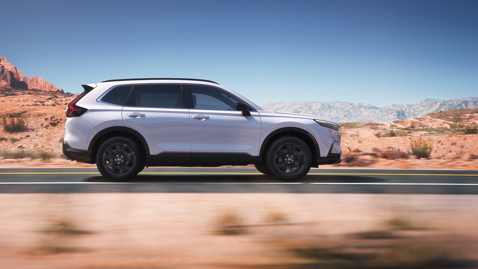 A silver Honda CR-V in profile, driving down the road in a desert
