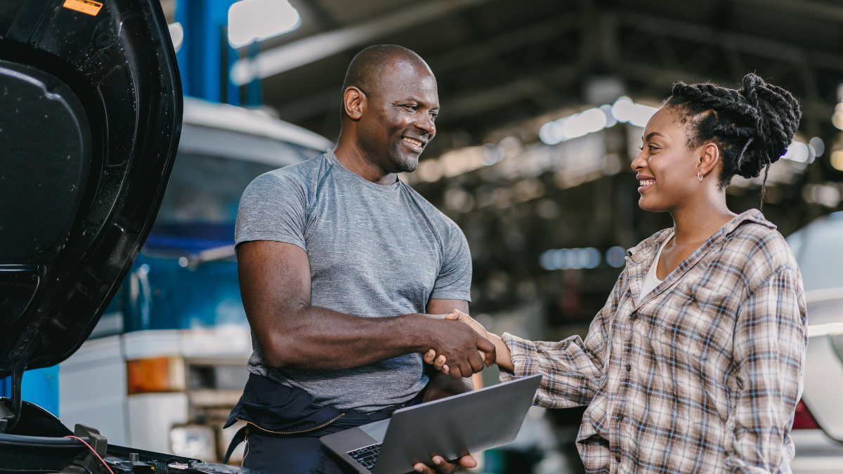 A woman customer shaking hands with an engineer holding a laptop after vehicle maintenance